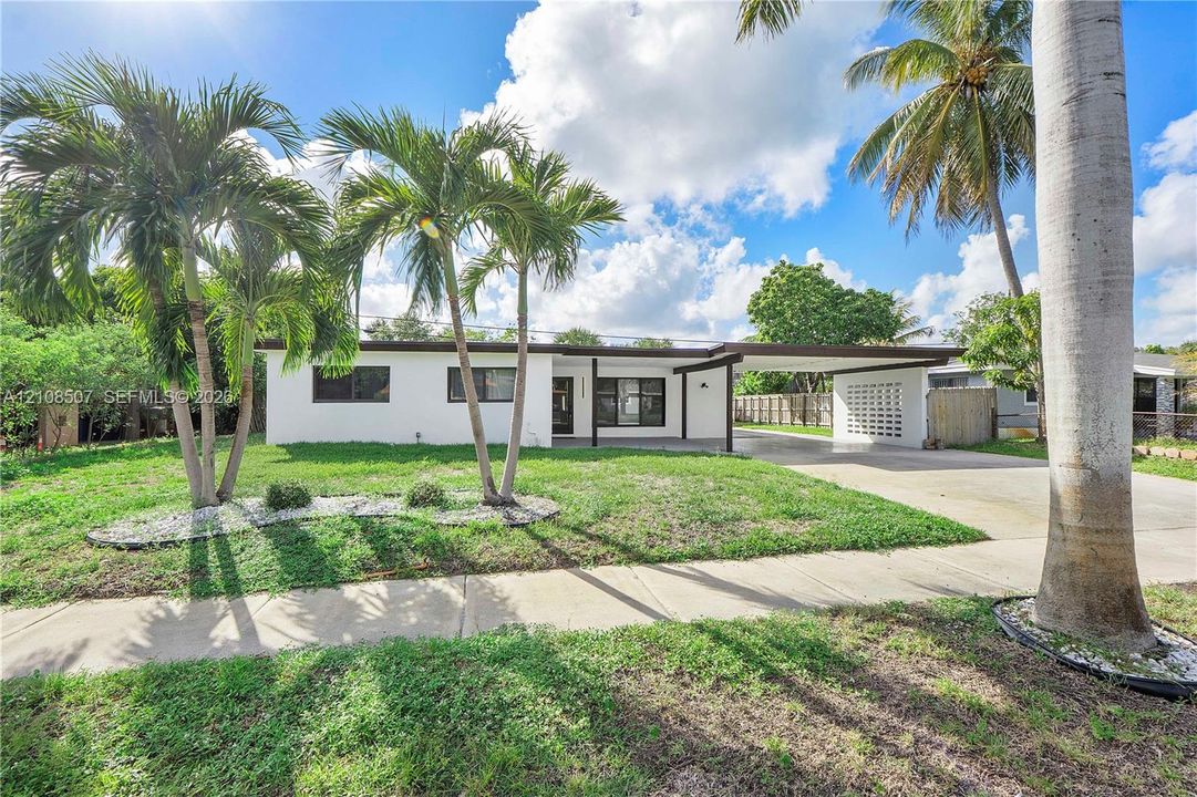 Single-story exterior featuring white stucco siding, a covered carport, decorative breezeblock wall accents, and mature palm trees