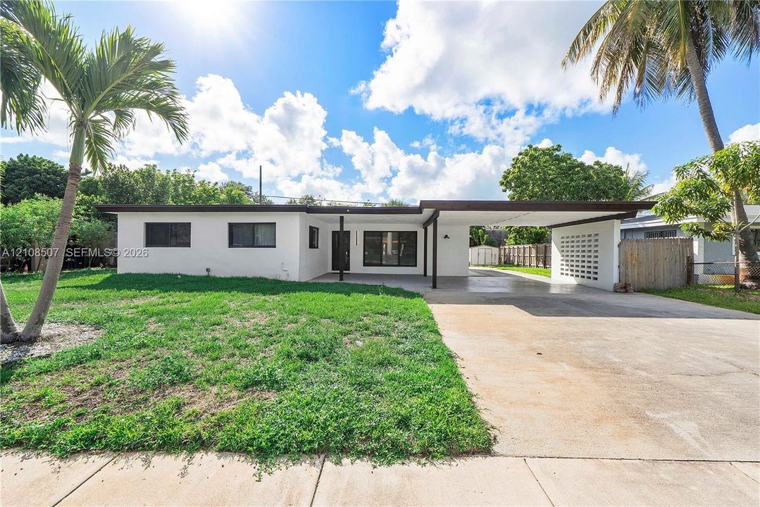 Single-story residence featuring a flat roofline, attached covered carport, decorative masonry screen wall, and concrete driveway