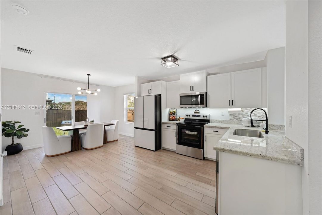 Kitchen featuring white shaker-style cabinetry, stone-finish countertops, stainless steel appliances, wood-finish tile flooring, and a multi-light fixture
