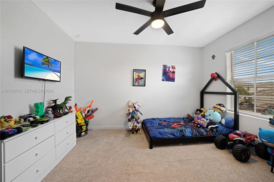 Neutral-toned interior space featuring wall-to-wall carpeting, a multi-blade ceiling fan with integrated lighting, and a large window with horizontal blinds