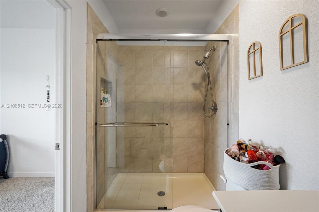 Shower enclosure featuring floor-to-ceiling neutral tile, a built-in recessed storage niche, a sliding glass door system, and a handheld shower fixture