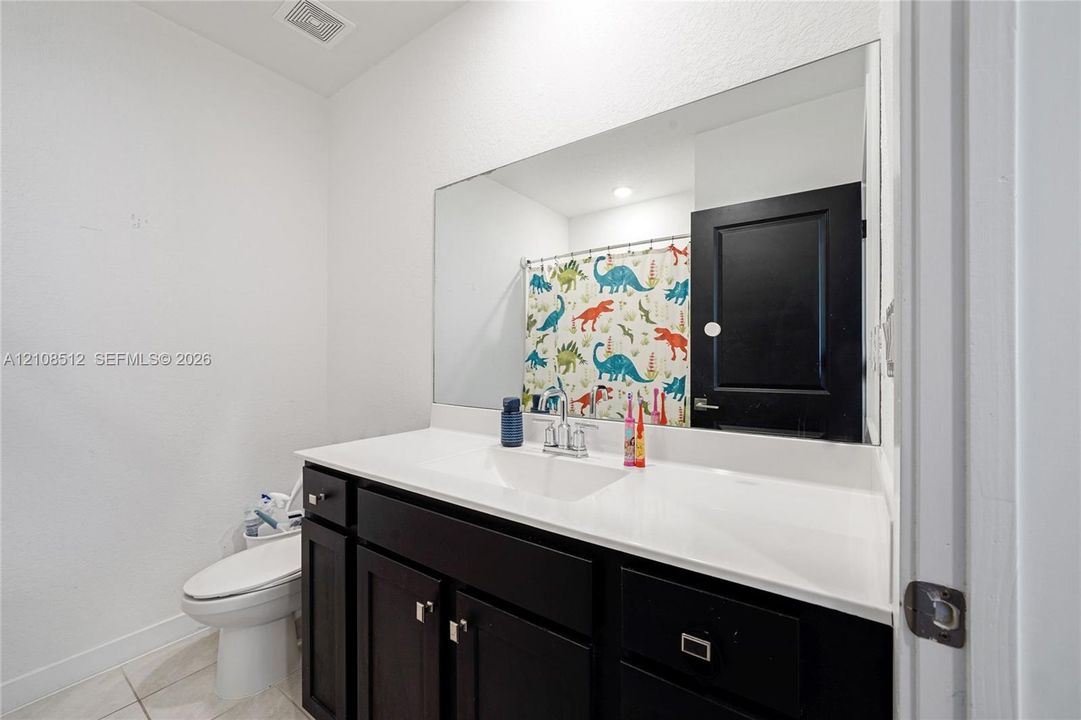 Dark-finish vanity cabinetry with a white integrated countertop, large wall-mounted mirror, and black-painted interior door