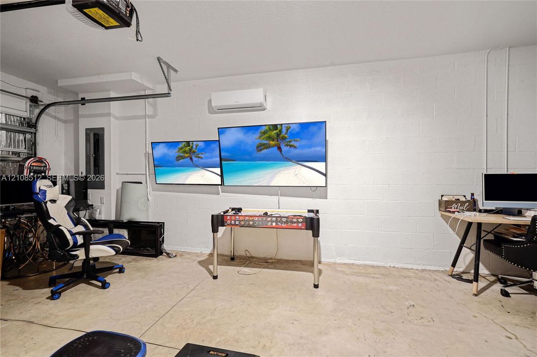 Finished garage featuring a concrete floor, painted masonry block walls, and a wall-mounted ductless heating and cooling unit