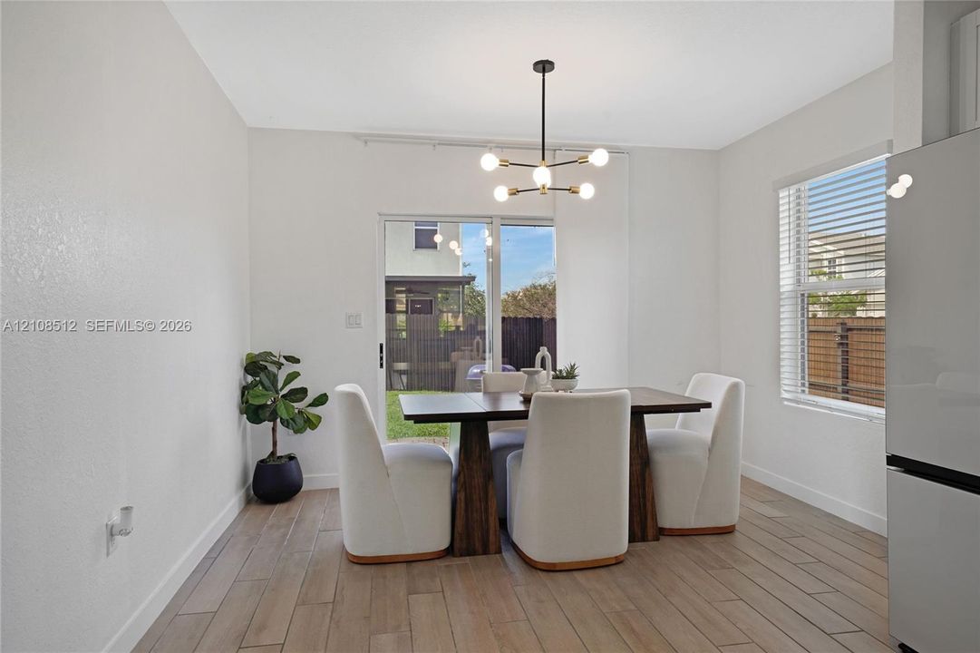 Dining area featuring wood-finish flooring, a modern six-light chandelier, a large window, and a sliding glass door providing external access