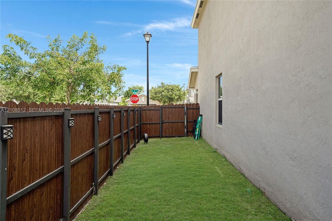 Stucco exterior wall with a private wood-style privacy fence, integrated post lighting, and a manicured grass lawn