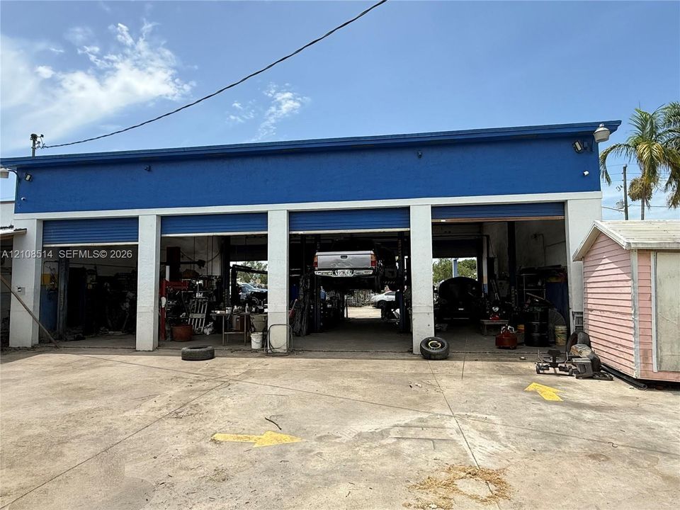 Commercial property featuring a concrete exterior, three open service bays with roll-up doors, and a paved exterior lot
