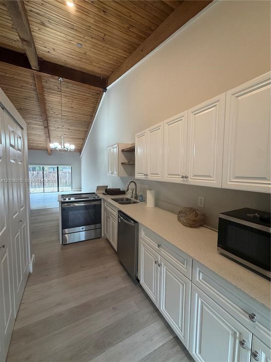 Vaulted ceiling with exposed wood beams, white cabinetry, solid-surface countertops, wood-finish flooring, and stainless steel appliances