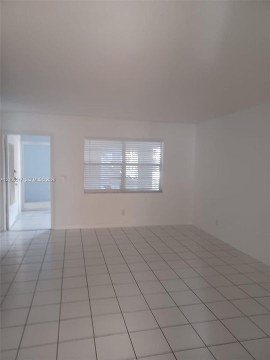 Neutral-toned interior space featuring white walls, large-format ceramic tile flooring, and a multi-pane window with horizontal blinds