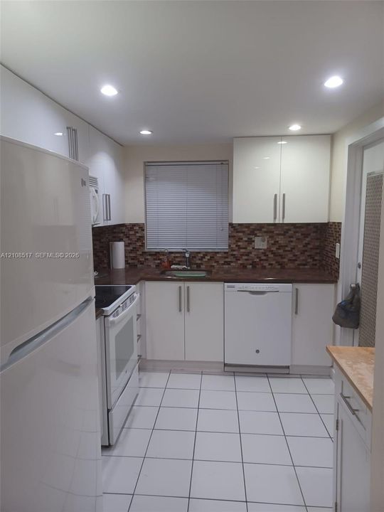 Kitchen featuring high-gloss white cabinetry, white ceramic tile flooring, a mosaic tile backsplash, and recessed ceiling lighting