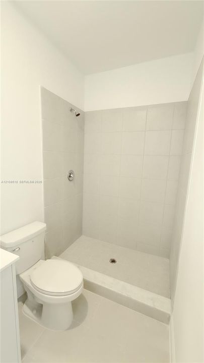 Walk-in shower with light-toned wall tile, porcelain shower basin, and chrome shower head