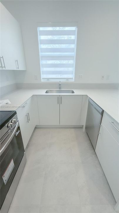 Kitchen featuring white flat-panel cabinetry, light-toned stone-finish countertops, stainless steel appliances, a stainless steel undermount sink, and tile flooring