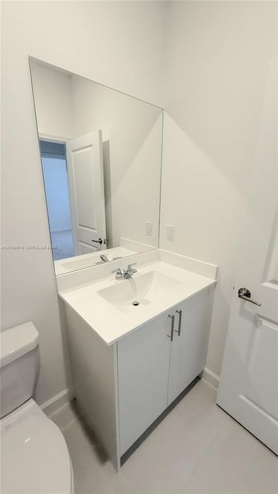 White vanity cabinet with a solid surface countertop, integrated sink, chrome dual-handle faucet, and full-length vanity mirror