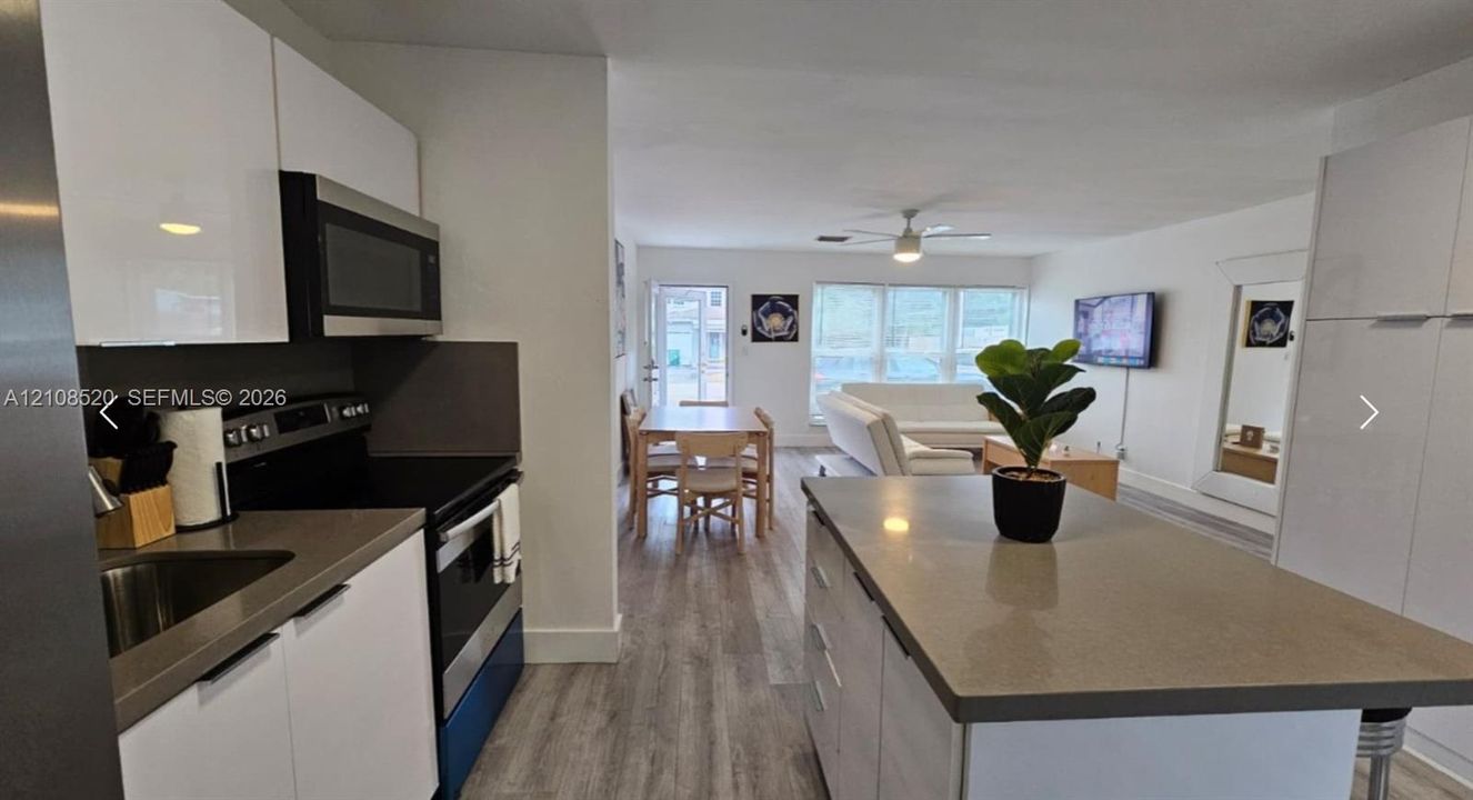 Kitchen featuring white gloss cabinetry, stone-finish countertops, stainless steel appliances, a central island, and wood-finish flooring