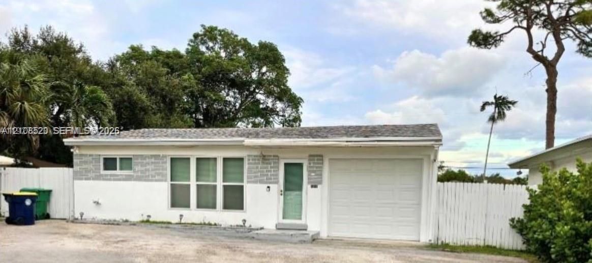 Single-story exterior featuring white stucco finish, decorative stone veneer accents, an attached one-car garage, and a white picket fence