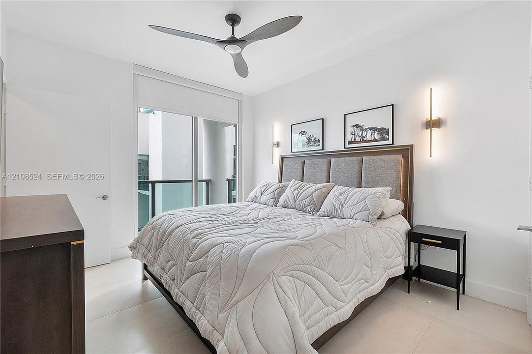 Minimalist interior featuring large-format tile flooring, dual vertical wall-mounted sconces, a matte black three-blade ceiling fan, and floor-to-ceiling glass sliding doors with access to a railed balcony