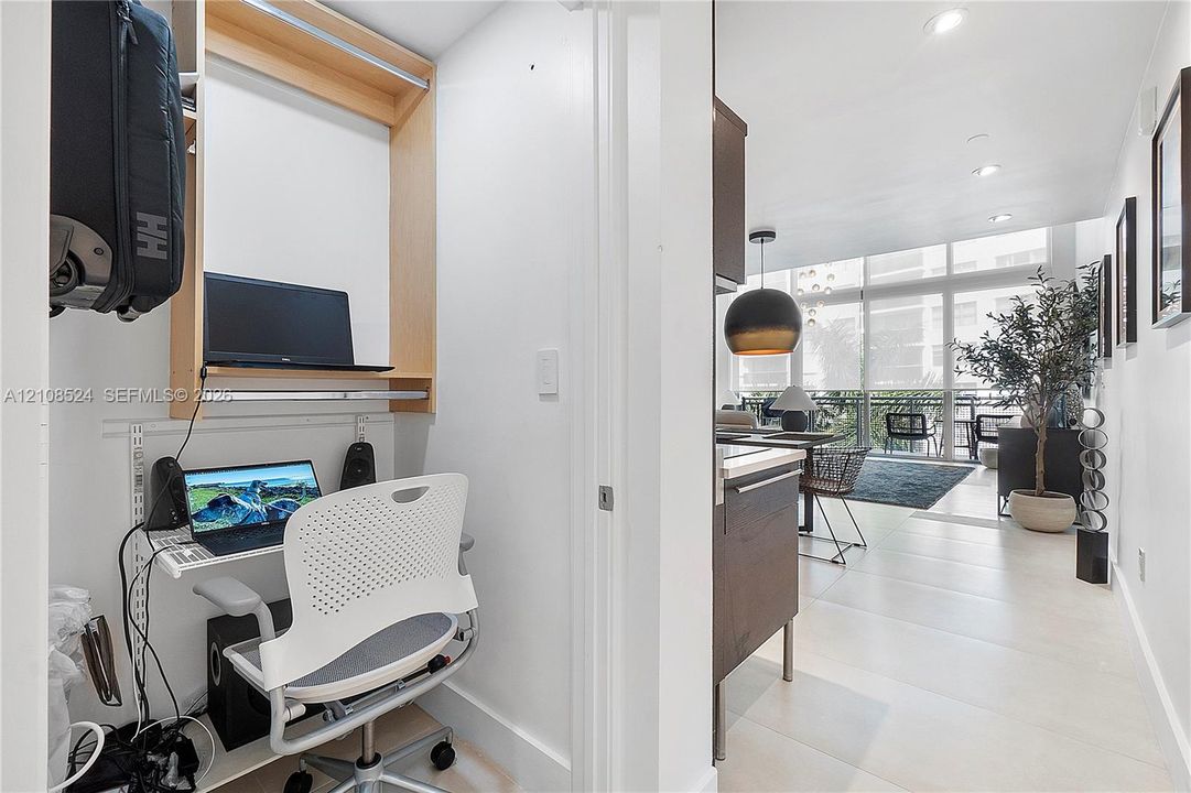 Built-in workstation featuring wood-finish shelving, large-format tile flooring, floor-to-ceiling glass wall panels, recessed lighting, and a pendant light fixture