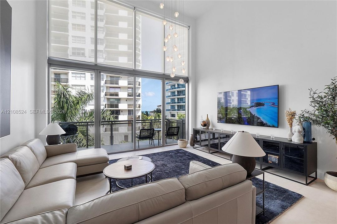 Double-height ceilings, floor-to-ceiling glass windows, recessed lighting, and a private balcony with a metal railing