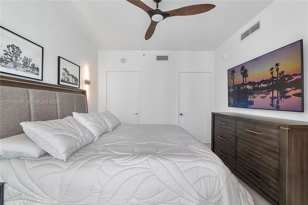 Bedroom featuring a floor-to-ceiling upholstered headboard, multi-blade ceiling fan, and solid-core interior doors