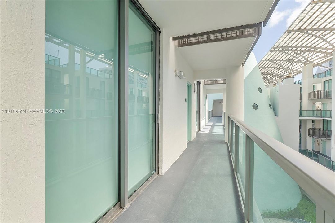 Covered balcony featuring full-height glass sliding doors, smooth concrete flooring, and a glass-panel railing