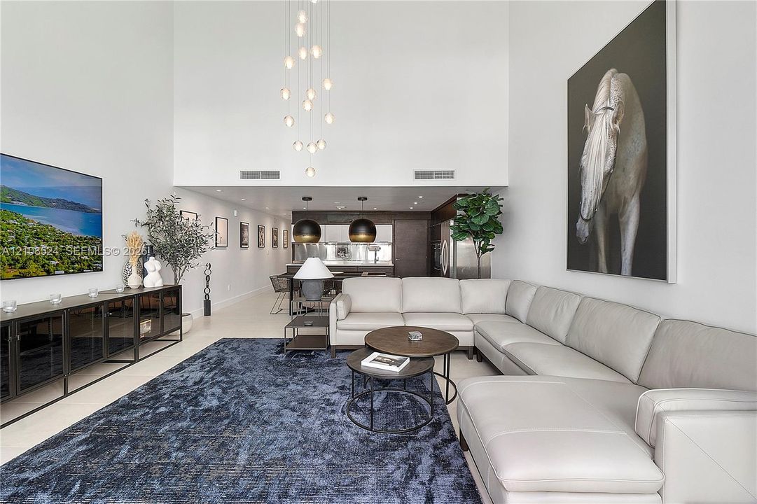 Expansive living area featuring double-height ceilings, floor-to-ceiling wall space, custom multi-tiered pendant lighting, and sleek dark-finish cabinetry