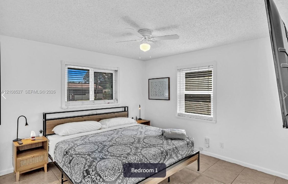 Neutral interior room featuring tile flooring, white walls, dual windows with integrated blinds, and a ceiling fan with light fixture