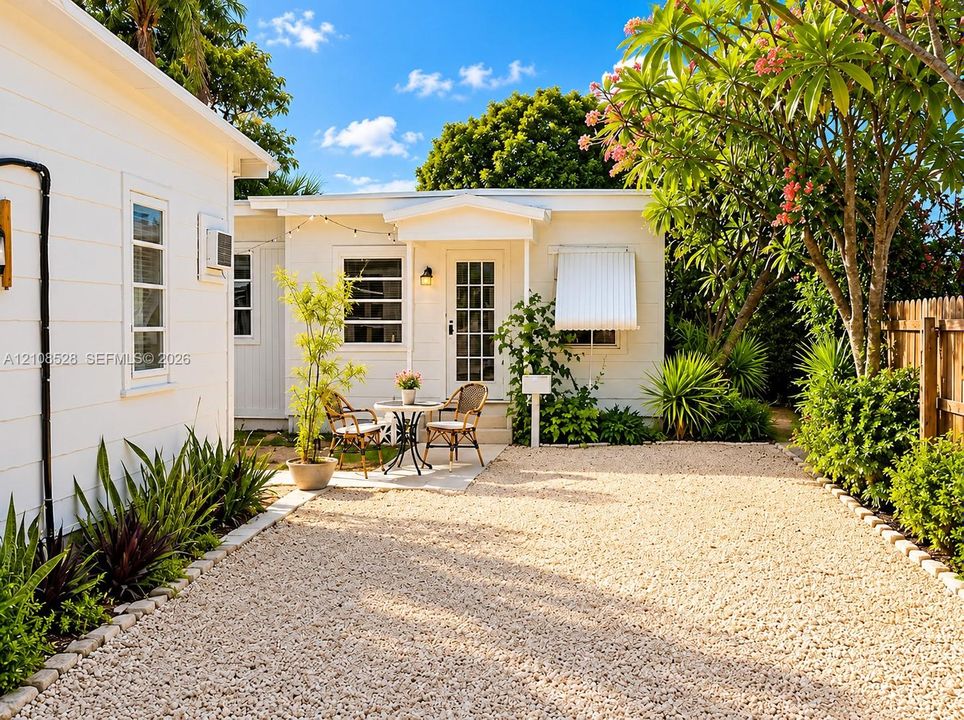 White horizontal siding exterior featuring a gravel courtyard, mature landscaping, and a glass-paneled entry door