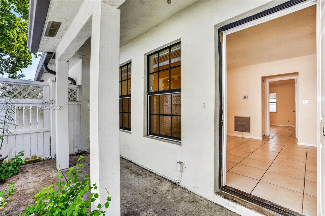 Covered exterior patio featuring a concrete floor, white structural columns, grid-patterned windows, and a white privacy fence