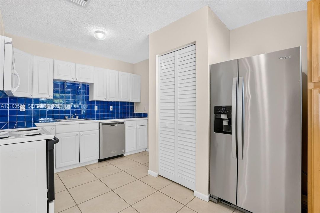 Kitchen featuring white cabinetry, blue tiled backsplash, stainless steel appliances, tile flooring, and a louvered pantry door