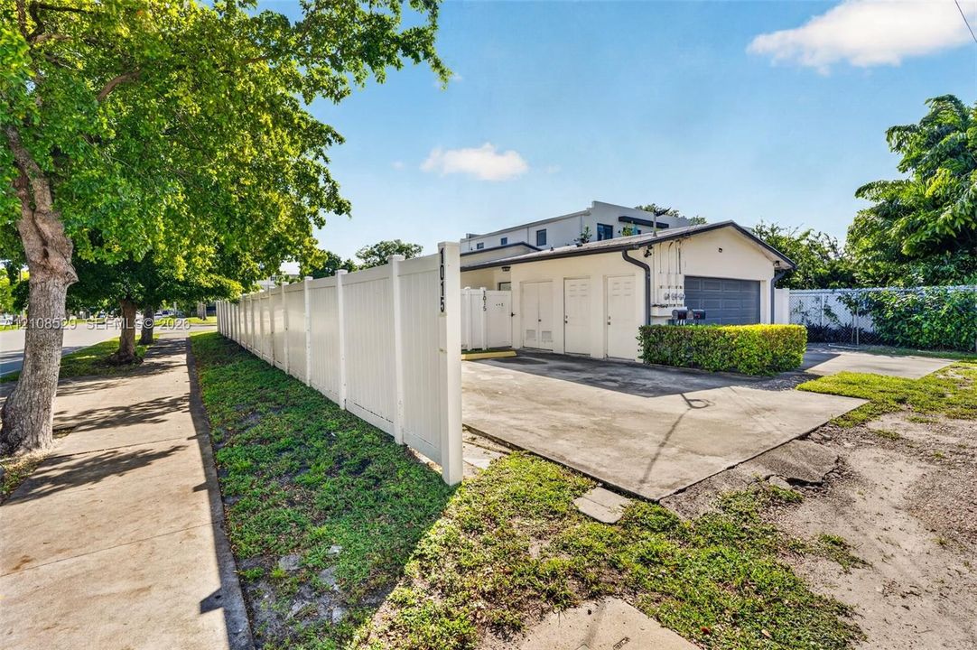 Concrete driveway leading to a multi-bay structure featuring a detached garage with solid-panel doors, secured by a white vinyl privacy fence