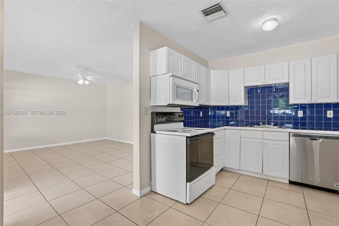 Kitchen featuring white cabinetry, blue tiled backsplash, stainless steel dishwasher, built-in microwave, and tile flooring