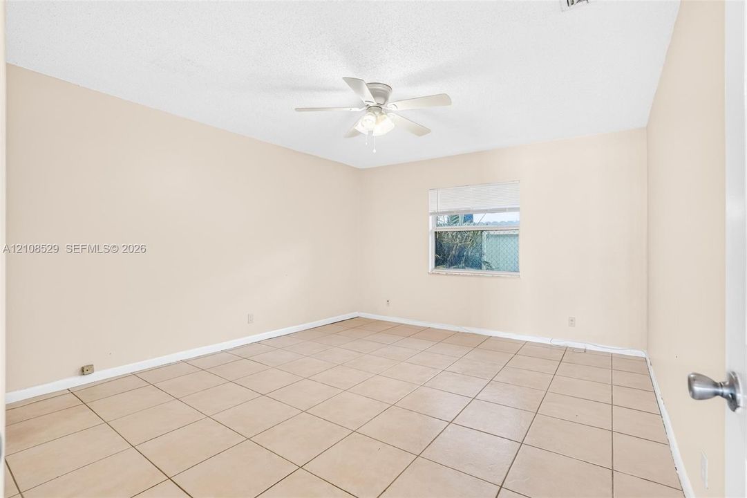 Neutral-toned interior space featuring ceramic tile flooring, a multi-blade ceiling fan with integrated lighting, and a single window with horizontal blinds