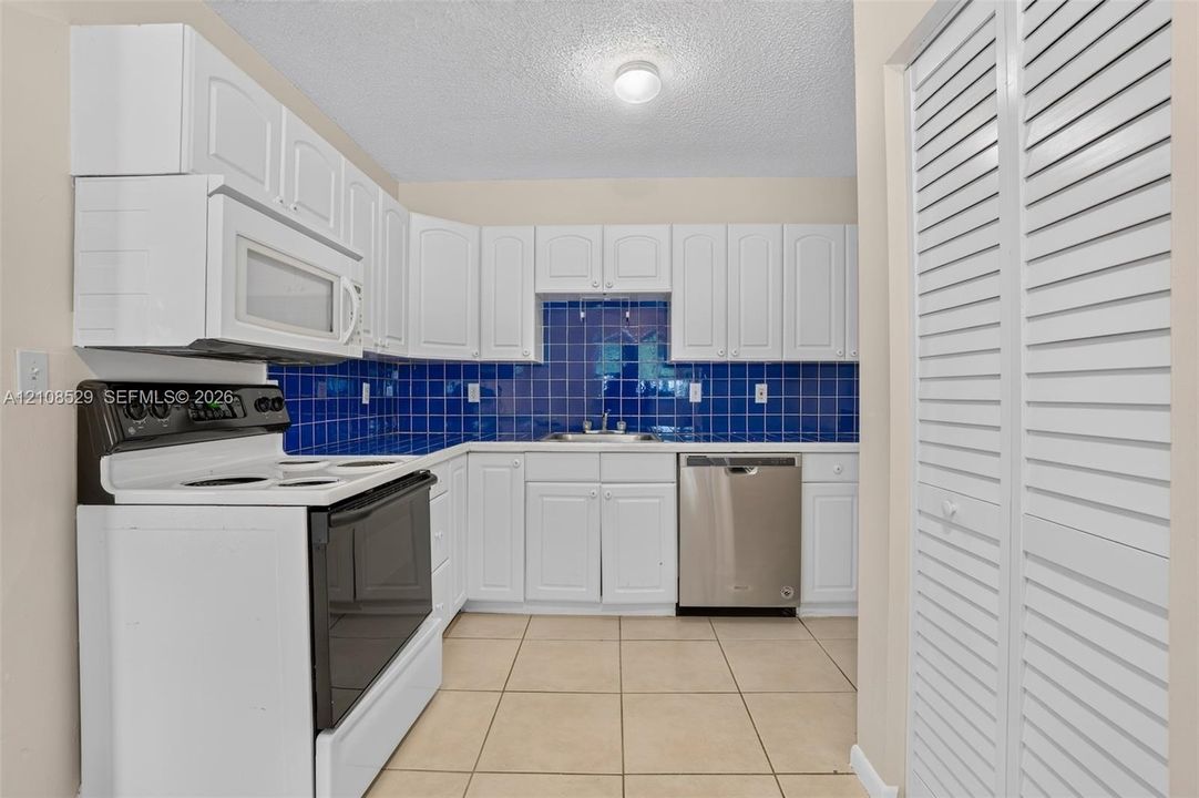 Kitchen featuring white cabinetry, blue tiled backsplash, stainless steel dishwasher, built-in microwave, and tile flooring