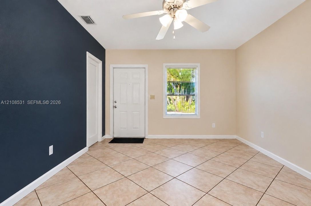 Room featuring diagonal tile flooring, a dark accent wall, a solid entry door, and a ceiling-mounted light fixture with integrated fan