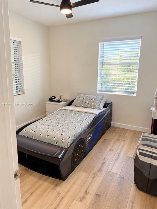 Room featuring wood-finish flooring, dual windows with horizontal blinds, and an integrated ceiling fan with light fixture