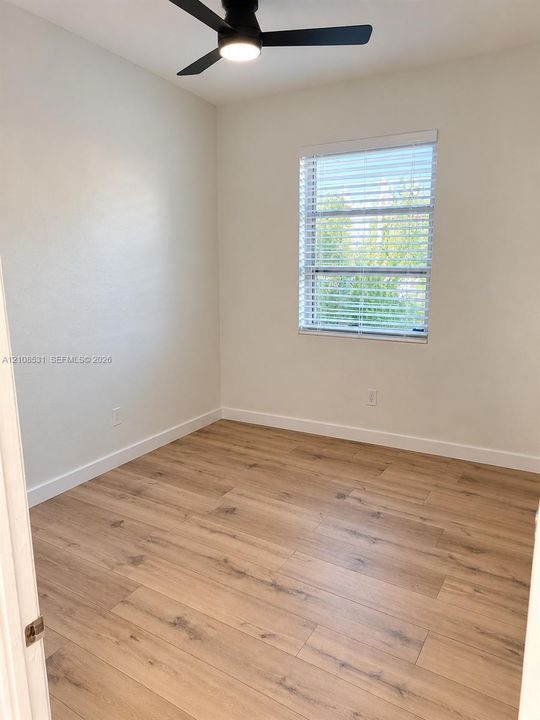 Room featuring wood-finish flooring, a matte black ceiling fan with integrated lighting, and a single-pane window with white horizontal blinds