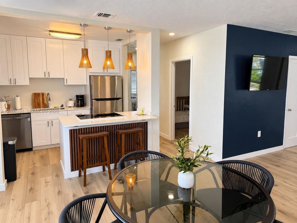 Kitchen featuring white cabinetry, quartz-surface countertops, stainless steel appliances, and a wood-slat breakfast bar accented by hanging pendant lighting