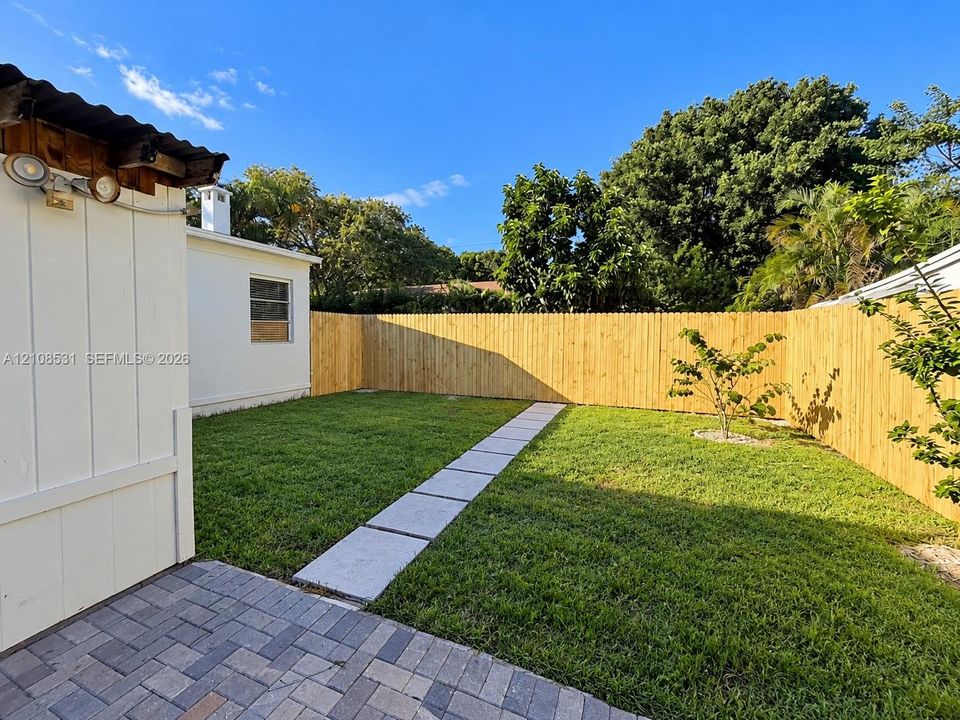 Private fenced yard featuring a brick paver patio, stone-finish walkway, and manicured lawn
