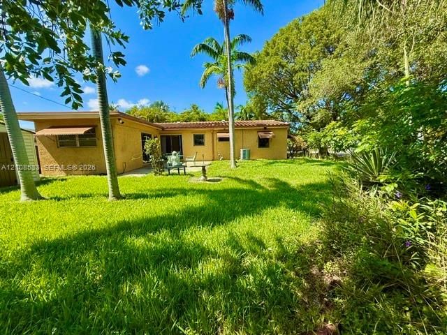 Rear exterior featuring a stucco facade, tile roof, concrete patio, and mature palm trees within a landscaped lawn