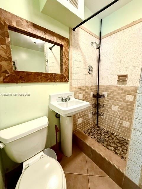 Pedestal sink with dual-handle faucet, shower enclosure with pebble tile flooring and tiled walls, and rectangular wall-mounted mirror