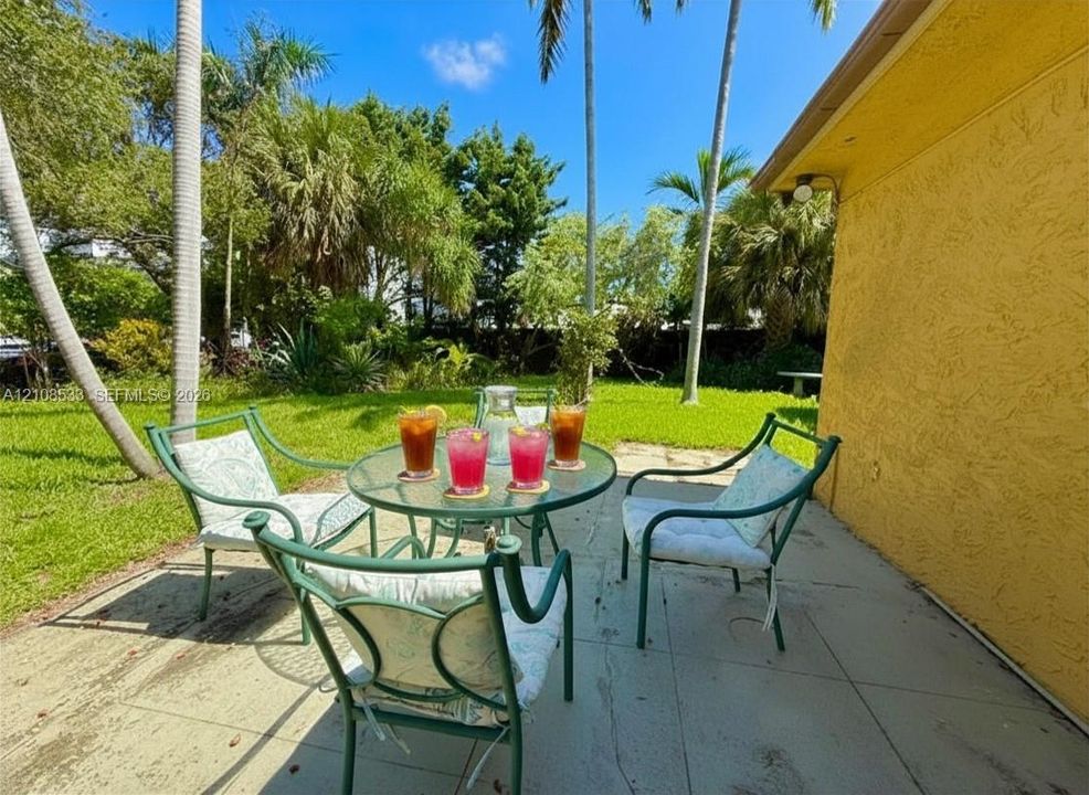 Rear patio featuring a concrete surface, texturized exterior wall, and established landscaping with palm trees