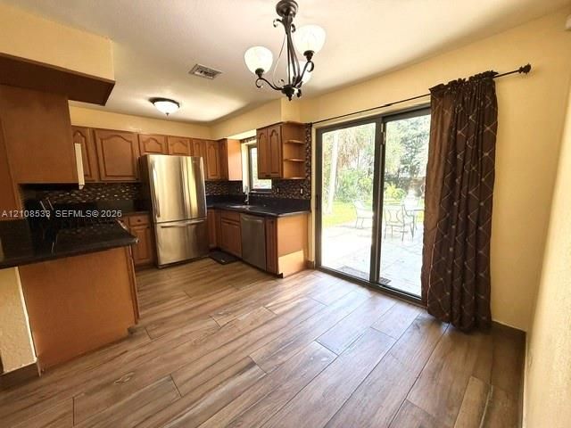 Kitchen featuring wood-finish flooring, dark stone countertops, stainless steel appliances, decorative light fixtures, and a glass sliding door