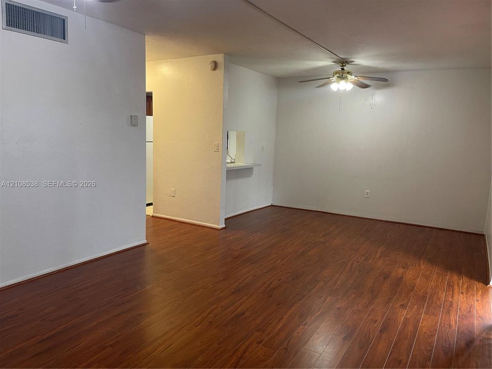 Living area featuring wood-finish flooring, ceiling fan with light fixture, and a pass-through opening