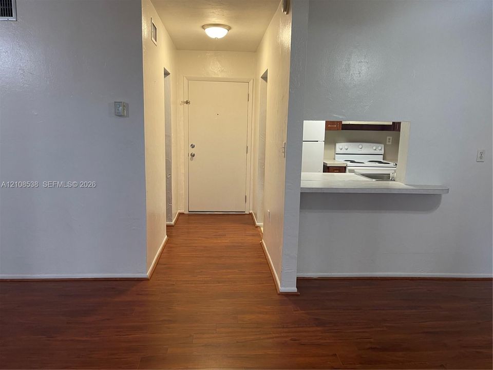 Entryway featuring wood-finish flooring, a solid-panel door with a peephole, and a kitchen pass-through with a built-in counter