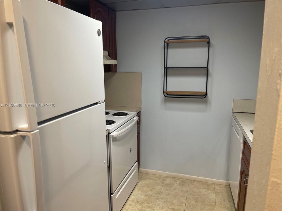 Kitchen featuring white appliance suite including a refrigerator, electric range, and dishwasher, paired with wood-finish cabinetry and neutral tile flooring