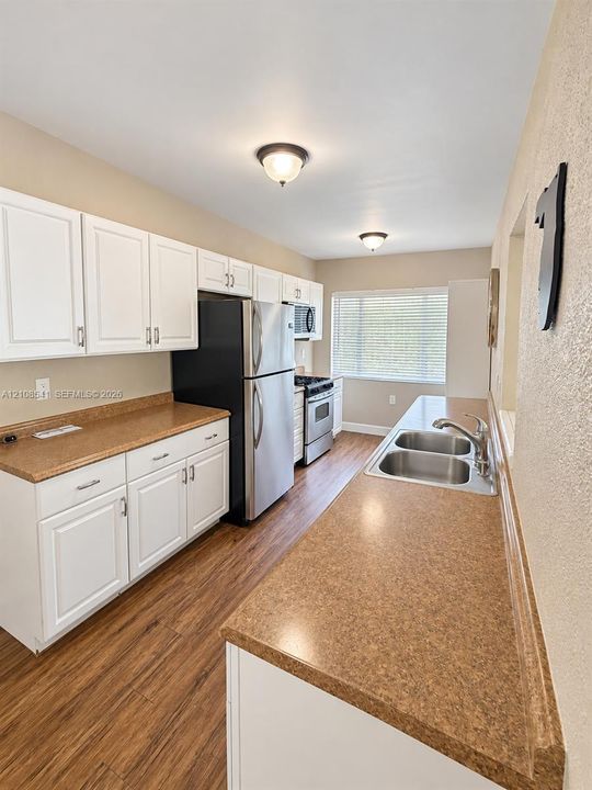 Kitchen featuring white shaker-style cabinetry, solid-surface countertops, wood-finish flooring, stainless steel appliances, and a dual-basin undermount sink