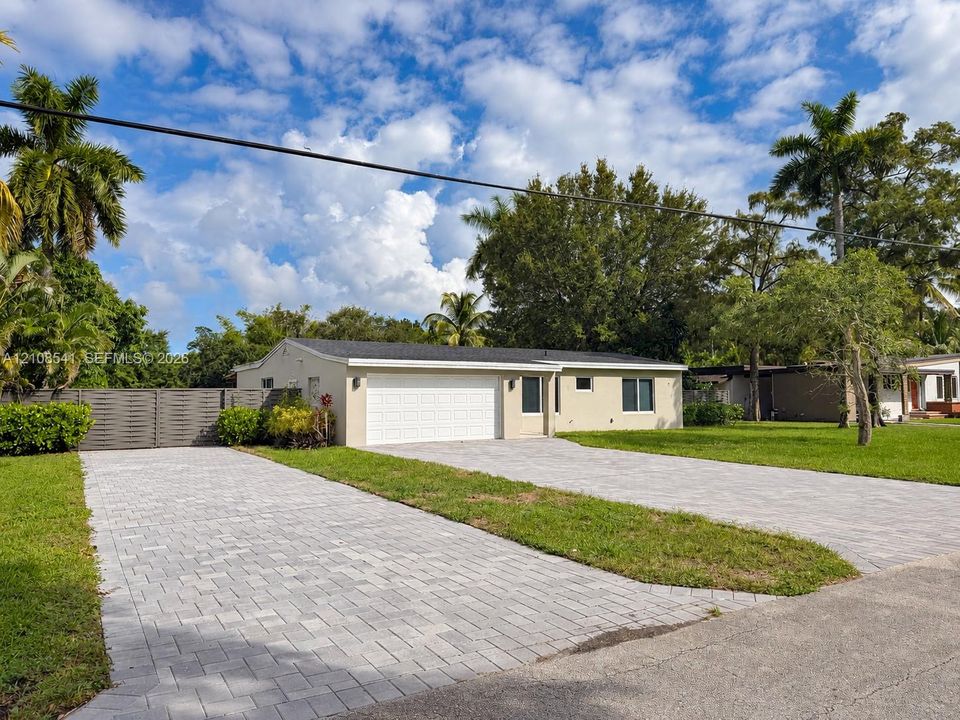 Single-story exterior featuring a paver driveway, an attached garage with a sectional door, and privacy fencing