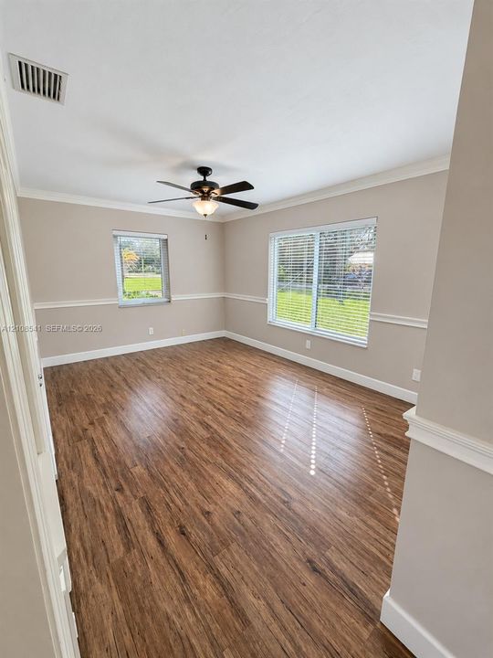 Room featuring wood-finish flooring, chair rail molding, crown molding, and a central ceiling fan with integrated lighting