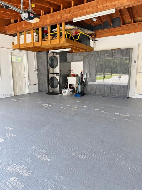 Garage featuring epoxy-coated flooring, ceiling-mounted storage loft, built-in floor-to-ceiling cabinetry, and a dedicated laundry area with a utility sink