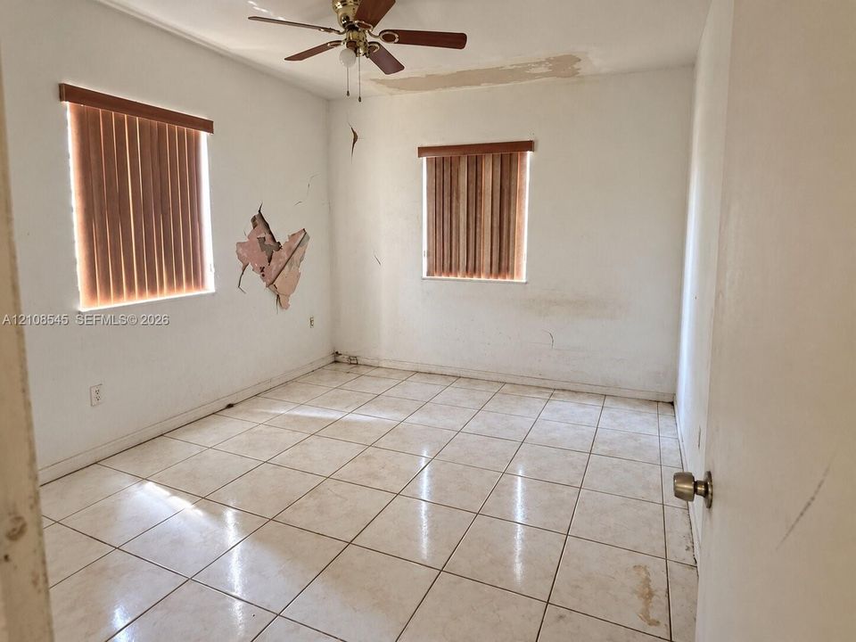 Ceramic tile flooring, dual windows with wood-tone vertical blinds, and a ceiling-mounted fan