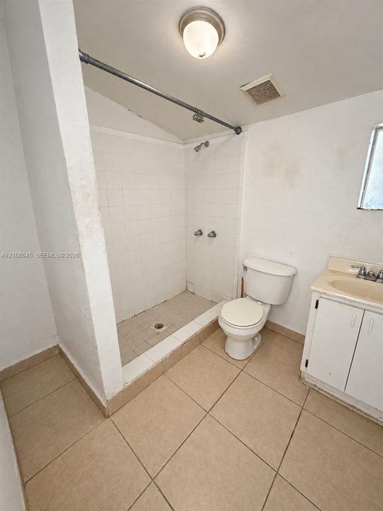 Bathroom featuring tile flooring, a tiled shower stall with a curtain rod, a standard toilet, and a vanity cabinet with an integrated basin